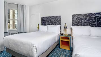 A hotel room with two beds, a window with curtains, a bedside table with a lamp, and a patterned headboard.