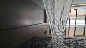 Un élément décoratif aquatique dans un espace intérieur moderne, avec un sol réfléchissant et une vue sur un bâtiment à travers de grandes fenêtres.