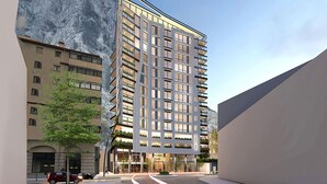 Un hôtel moderne à plusieurs étages, doté d’une façade en verre, situé en milieu urbain avec une chaîne de montagnes en arrière-plan.