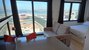Une chambre d’hôtel moderne dotée d’une grande fenêtre donnant sur la ville, d’un canapé, d’un lit et d’une petite table.