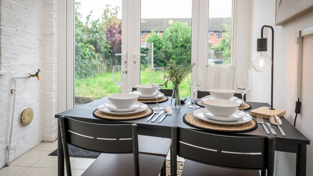 Mesa de comedor preparada para cuatro personas, con platos blancos, cubiertos y un candelabro como centro de mesa.