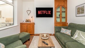 Una sala de estar con un sofá verde, una mesa de centro de madera y un televisor que muestra "NETFLIX".