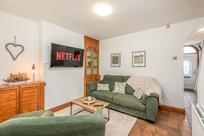 Uma sala de estar com um sofá verde, uma mesa de centro, uma TV fixada na parede e um armário de madeira.