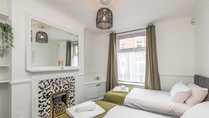 Habitación de hotel con chimenea, dos camas, un espejo grande y una ventana con cortinas.