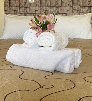 A neatly made bed with rolled white towels and a small bouquet of pink flowers on top. - Cachoeira dos Luis Parque e Pousada (Bueno Brandão)