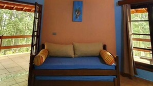 Una habitación con una cama, una lámpara en la pared y una ventana con vista a árboles.