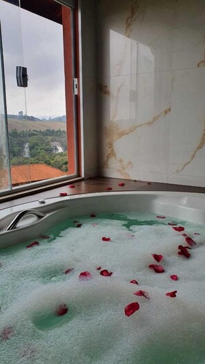 Una bañera con pétalos de rosa, puerta de cristal y vista a un paisaje.