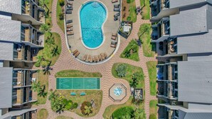 Vue aérienne d’un hôtel moderne doté d’une piscine centrale, d’espaces de détente en plein air et d’un court de tennis.