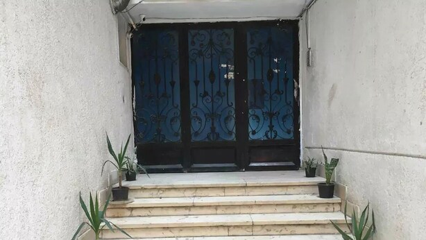 Unos escalones de piedra conducen a una puerta de metal negro con diseños decorativos.