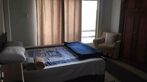 Un dormitorio con una cama, una silla, un armario y una ventana con cortinas.