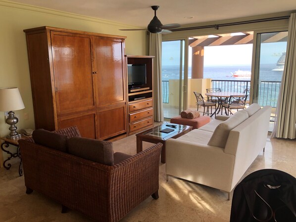 Habitación de hotel con un amplio armario de madera, televisión, sofá y zona de comedor con vistas al mar.