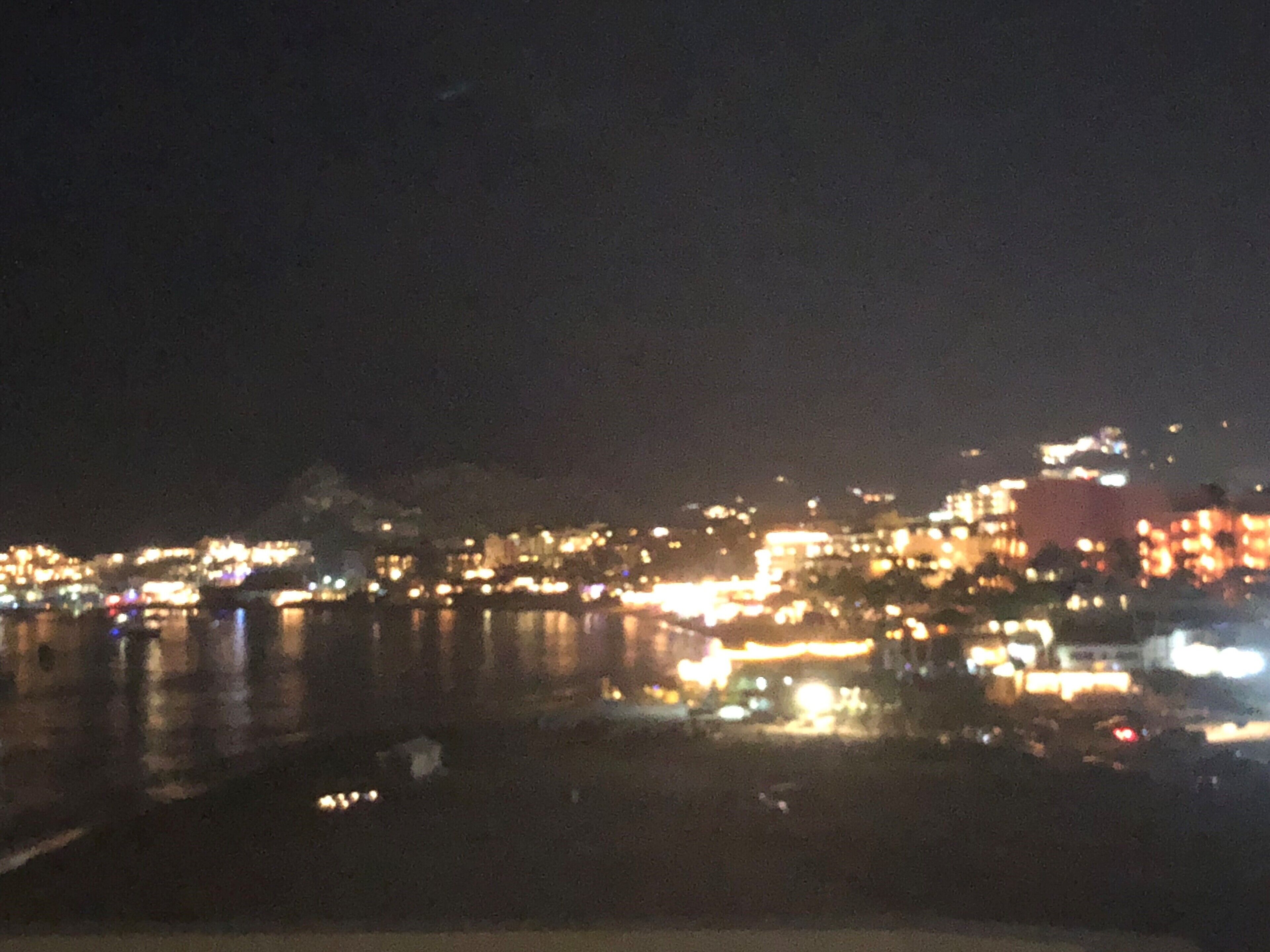 A nighttime cityscape with illuminated buildings and a body of water.