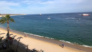 A beach with a palm tree, people on the sand, and boats in the water.