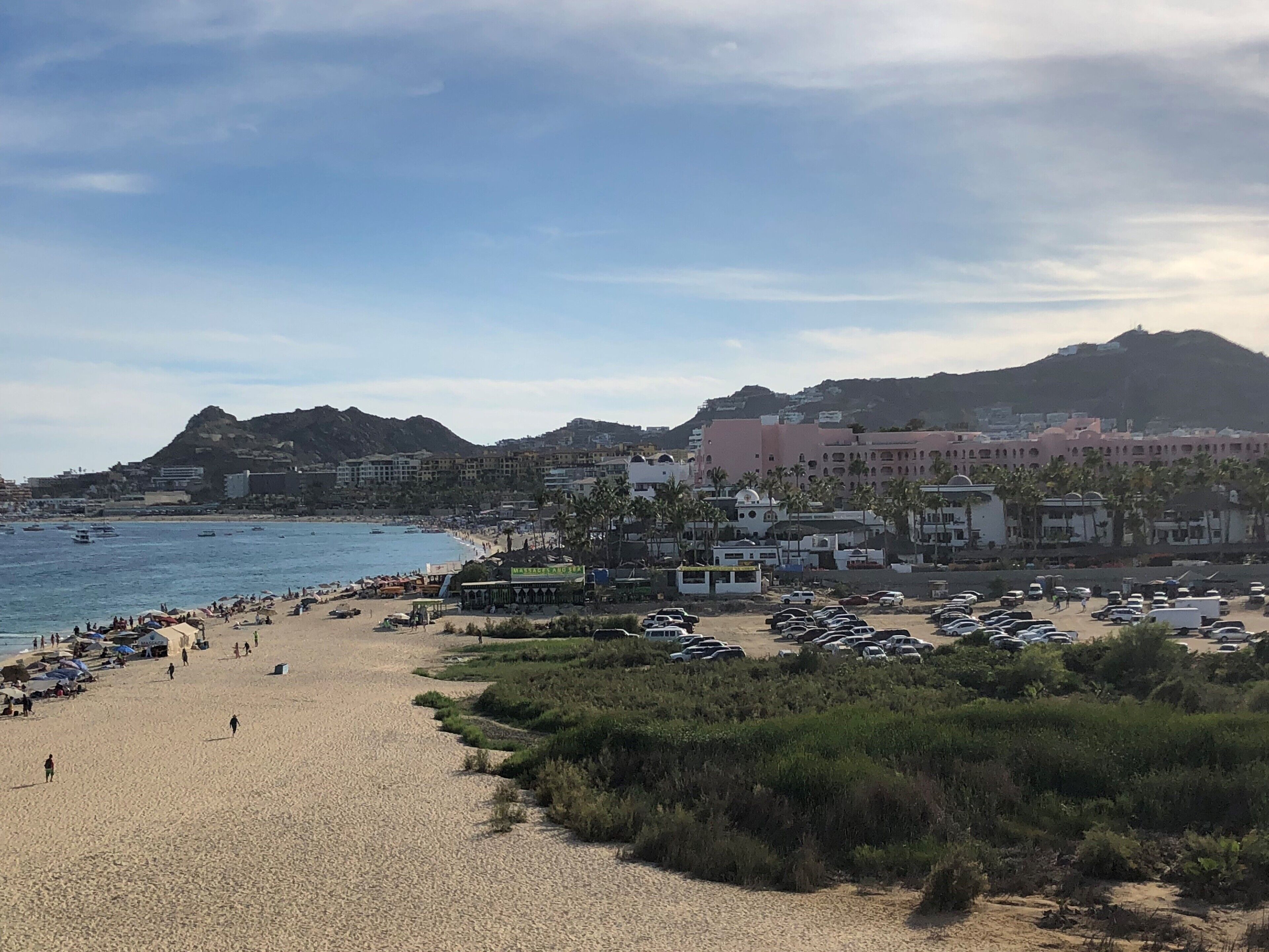 Ein Strand mit Parkplatz, Strandbesuchern und Gebäuden im Hintergrund.