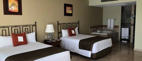 A hotel room with two beds, a nightstand, a lamp, a ceiling fan, and a bathroom visible through an open door.