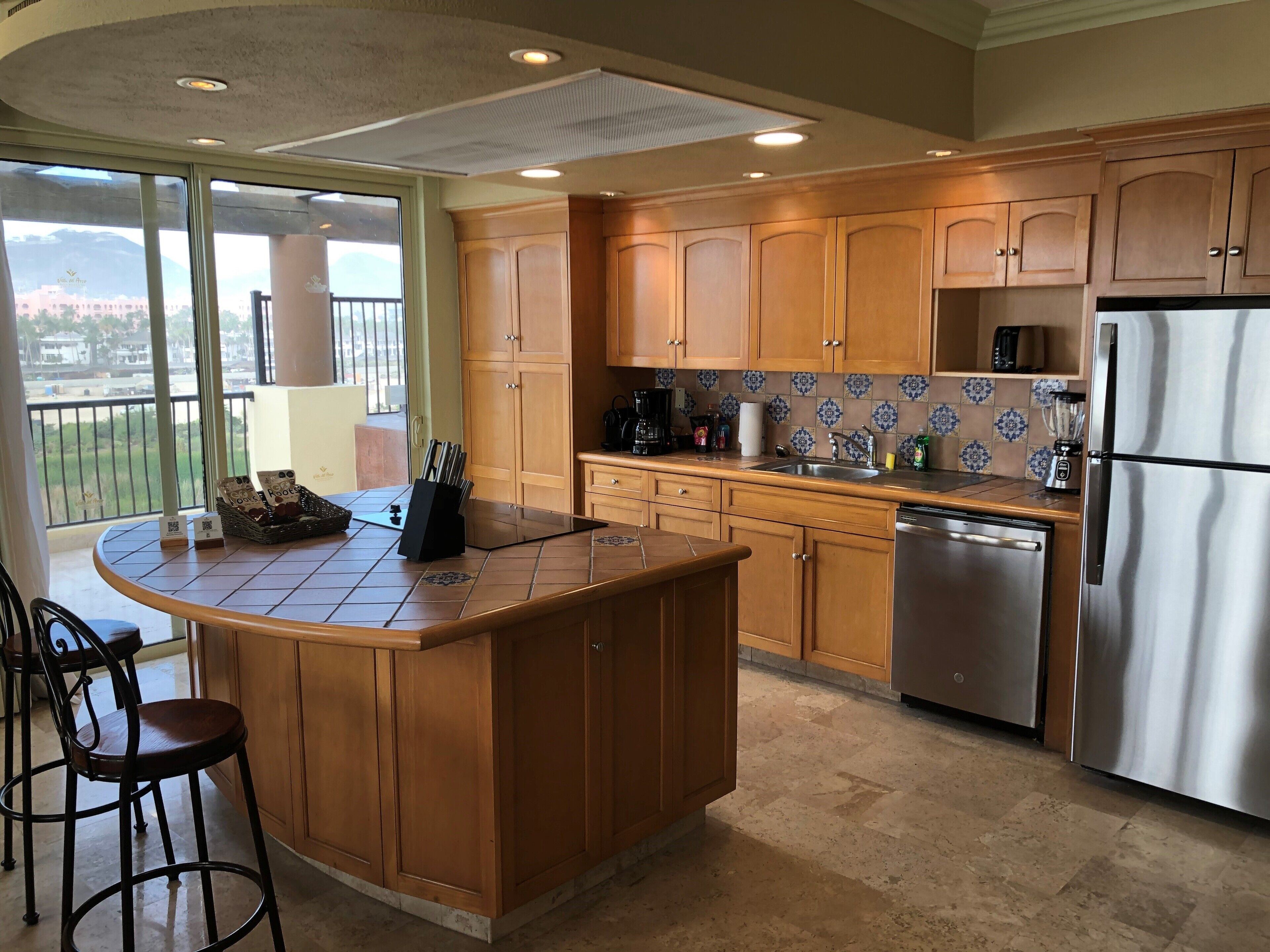A modern kitchen with wooden cabinets, a stainless steel refrigerator, and a large island with bar stools.