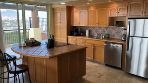 A modern kitchen with wooden cabinets, a stainless steel refrigerator, and a large island with bar stools.