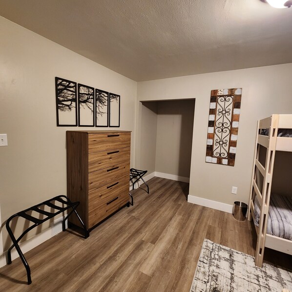 A room with a wooden dresser, a bunk bed, a small table, and a wall with three framed pictures.