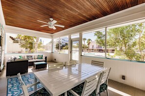 A sunlit room with a wooden ceiling, large windows, a white table, and a sofa with cushions. - Private Resort Across street from beach (Siesta Key)