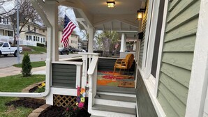A front porch with a 'hello' mat, a flag, and a chair.