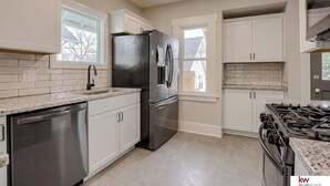 A modern kitchen with white cabinetry, a stainless steel refrigerator, a dishwasher, and a gas stove.