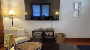 A living room with a sofa, a television mounted on the wall, a table with a woven basket, and two side tables with baskets.