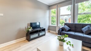 Un salon moderne avec un canapé gris, un meuble de rangement noir pour appareils électroniques et une table basse blanche.