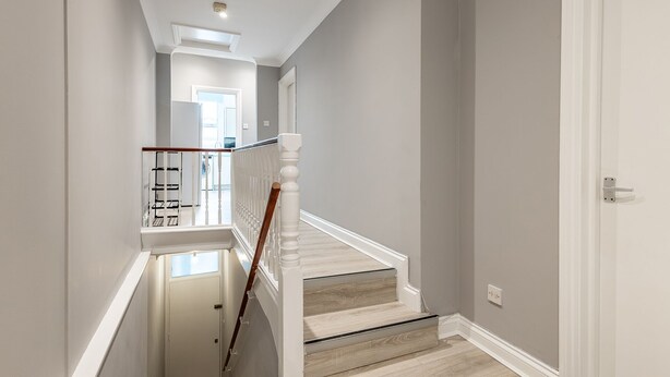 Un escalier avec des rampes blanches et une main courante en bois menant à une porte.