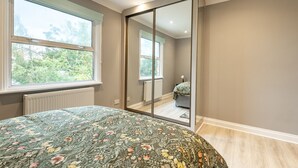 Une chambre à coucher comprenant un lit, une grande fenêtre, un radiateur et une porte coulissante donnant sur une autre pièce.