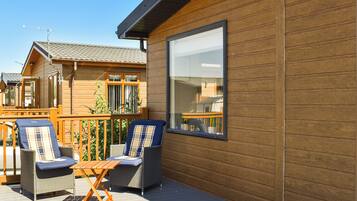 Une terrasse en bois avec deux fauteuils en osier et une petite table, donnant sur un quartier résidentiel avec des maisons et un ciel dégagé.