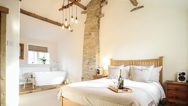 Une chambre avec un grand lit, une tête de lit en bois, un mur en pierre et un plancher en bois.