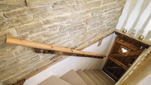 Un escalier en bois, avec un mur en pierre en arrière-plan, une main courante en bois et une petite étagère sur laquelle sont posées des bougies.