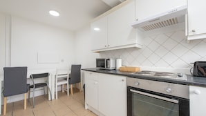 Una cucina con mobili bianchi, un fornello, un forno a microonde e un'area pranzo con sedie e un tavolo.