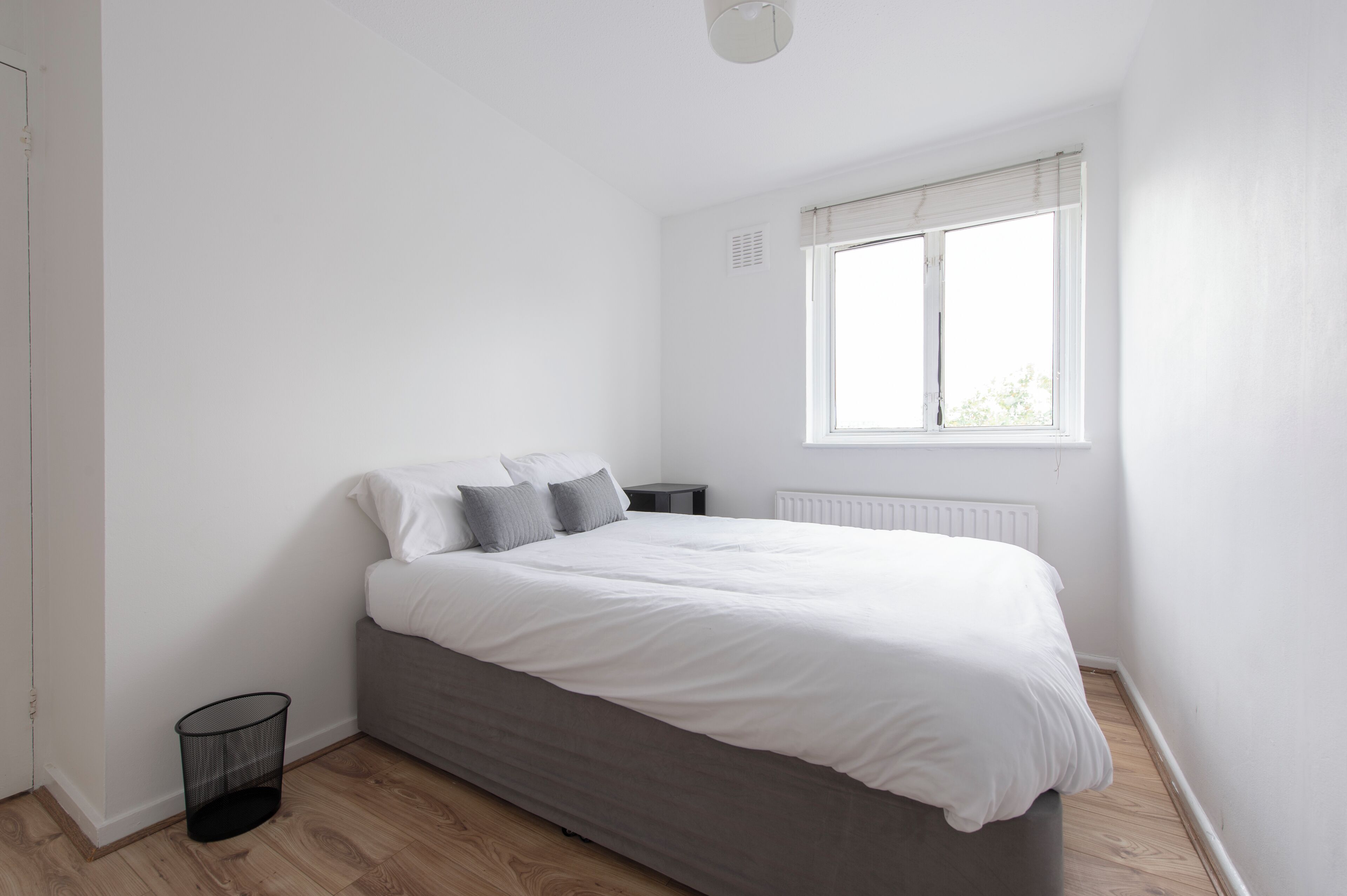 Quarto com cama, janela, radiador e um cesto de lixo.