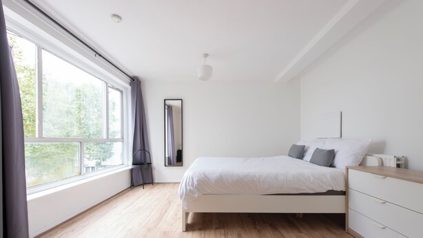 Una camera da letto con un letto, una cassettiera, uno specchio e una finestra con tende.