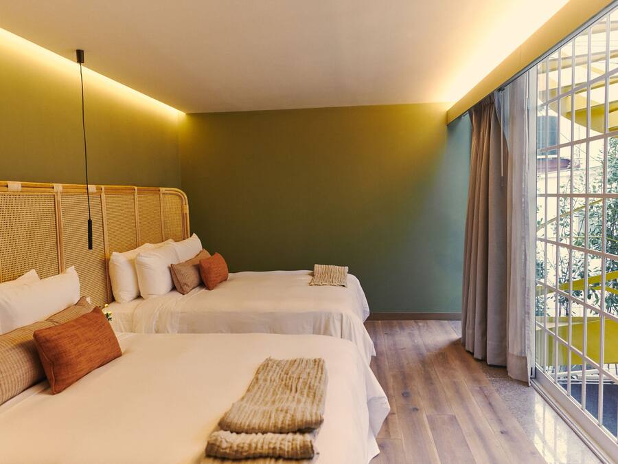 A hotel room with two beds, a large window with curtains, and a view of greenery outside.