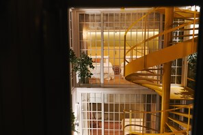 Una escalera de caracol con barandilla amarilla en una habitación luminosa con ventanales amplios.