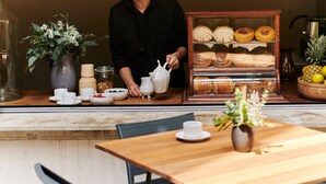 A cafe with a wooden counter, a display case of pastries, and a table with a vase of flowers. - Casa Izeba - Luxury Guest House (Mexico City)