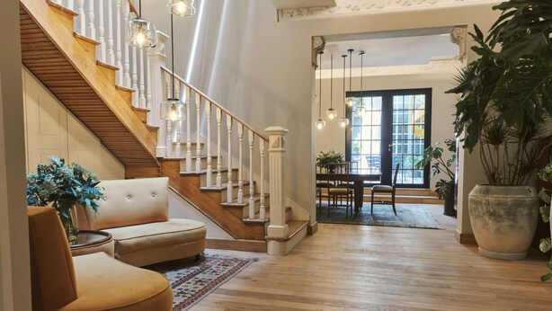 A spacious living room with a wooden staircase, a beige sofa, and a large potted plant. - Casa Izeba - Luxury Guest House (Mexico City)