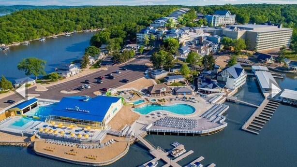 Vista aérea de un hotel frente al mar con una gran piscina, varios edificios y barcos amarrados.