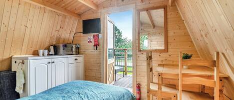 Una cabaña de madera acogedora con kitchenette, una cama con colcha estampada en azul y un banco de madera.