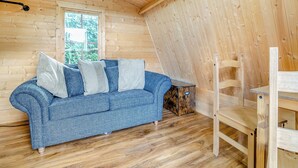 A wooden cabin interior with a blue sofa, wooden flooring, and a window.