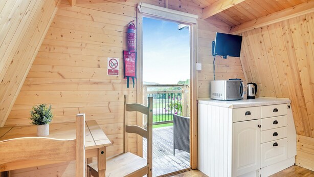 A wooden interior with a dining table and chairs, a kitchenette with a microwave and kettle, a fire extinguisher, and a 'No Smoking' sign.