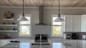 A modern kitchen with a central island, pendant lights, and a view of the outdoors through windows.