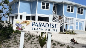 A beach house named Paradise with a blue exterior, a covered porch, and a sign featuring marine life.