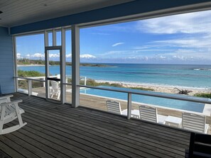 Terraza de madera con piscina y sillas, con vista a una playa y al océano.