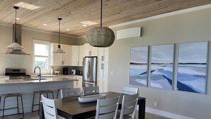 A modern kitchen with a central island, stainless steel appliances, pendant lighting, and artwork on the walls.