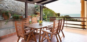 Una mesa y sillas de madera en un balcón con un muro de piedra y plantas en macetas.