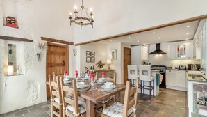 A dining area with a wooden table set for four, a chandelier, and a kitchen in the background. - The Coach House - UK45027 (Crickhowell)