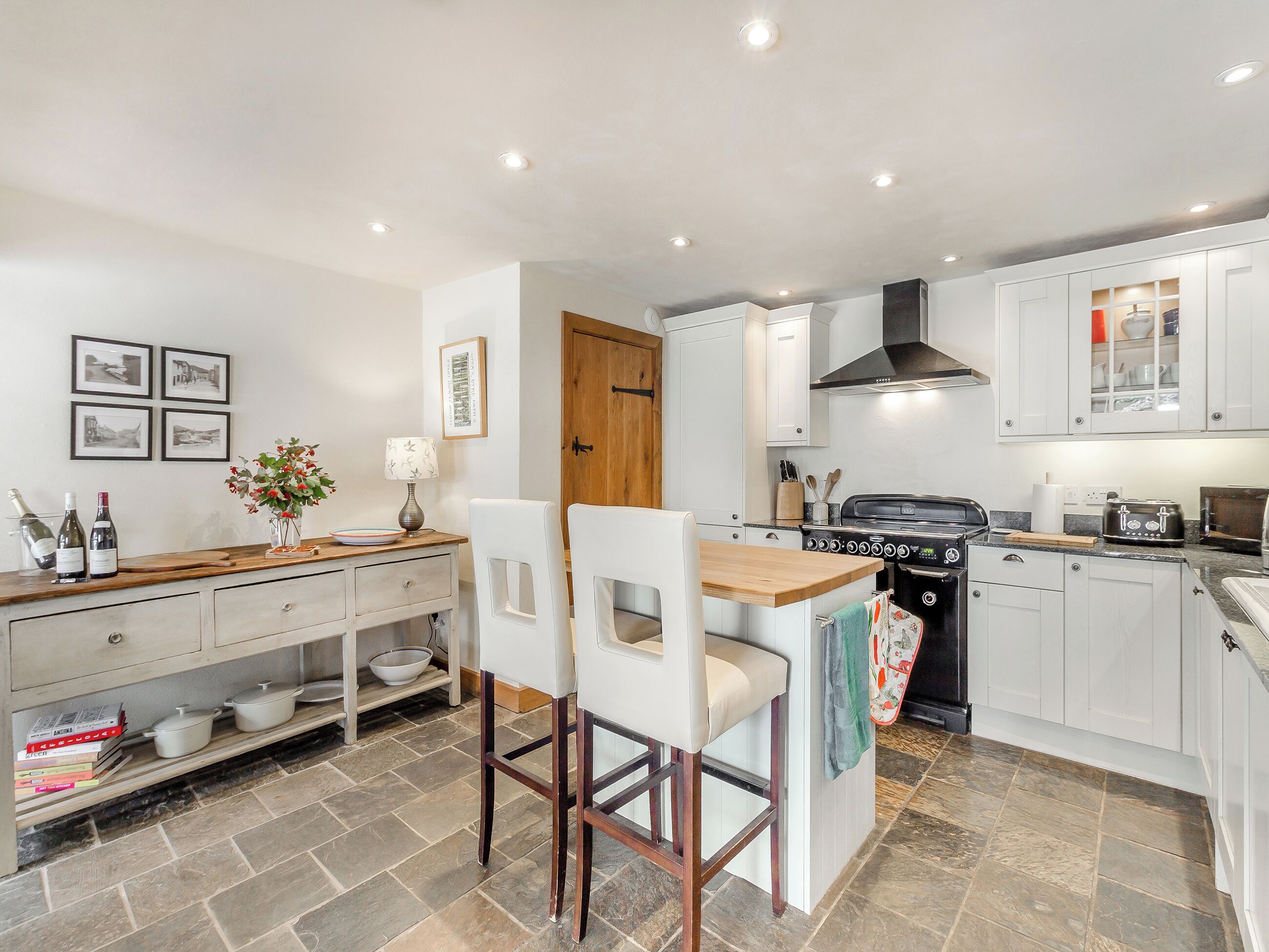 A modern kitchen with white cabinets, a wooden countertop, a stove, and a dining area with two chairs.